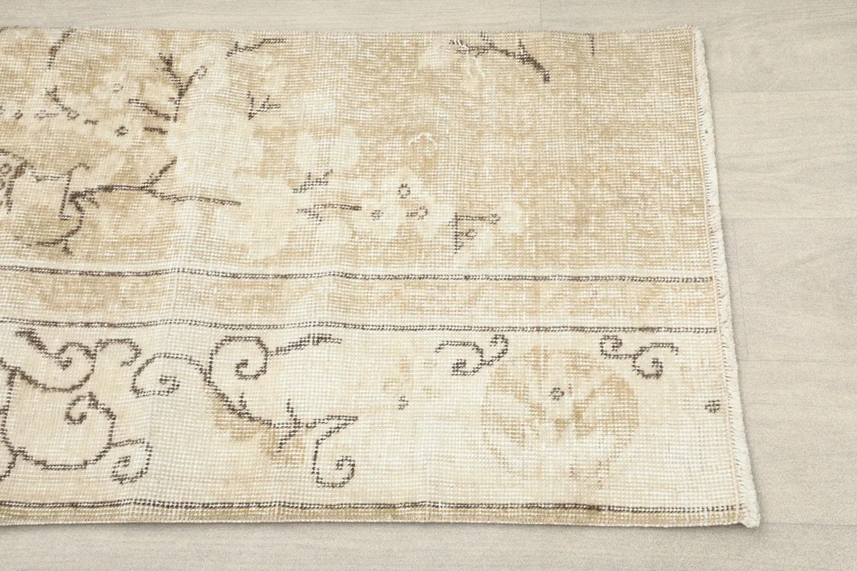 Close-up detail of the rug's corner, showing the beige field and brown vine motifs.
