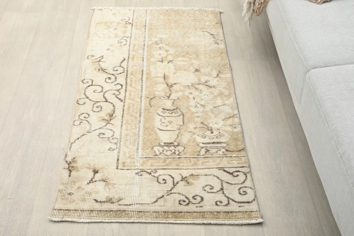 Vintage beige and ivory Anatolian rug with brown floral and vase motifs, viewed from an angle in a room
