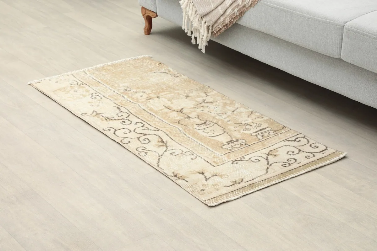 Close-up angled view of the beige and brown vintage rug on a light floor next to a sofa