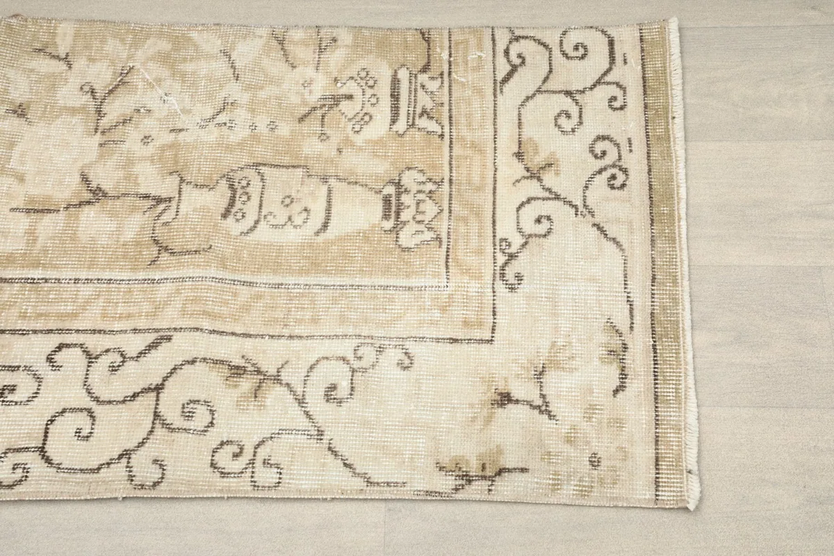 Detailed view of the corner of the rug, showing the scrolling border and floral patterns in brown on a beige field