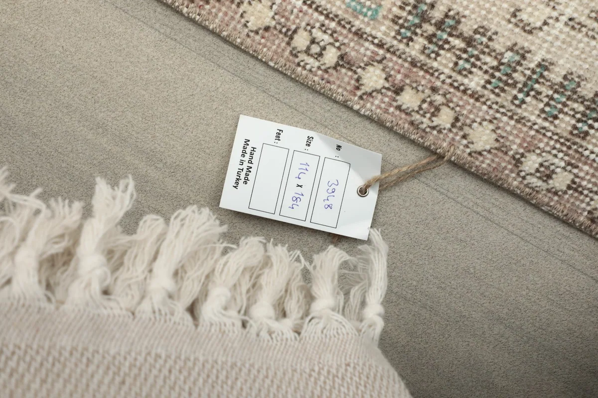 Close-up of the rug's fringe and a size tag showing dimensions 114 x 184 cm.