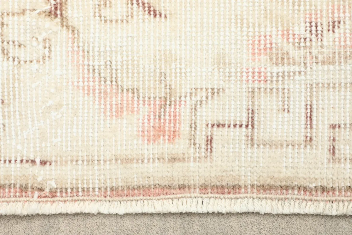 Close-up detail of the low wool pile texture and faded rose and beige colors of the rug.
