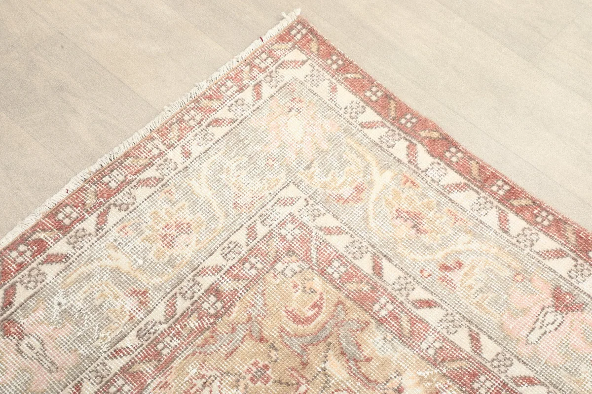 Corner detail of the rug's border, showing the rust and beige patterns and slight wear