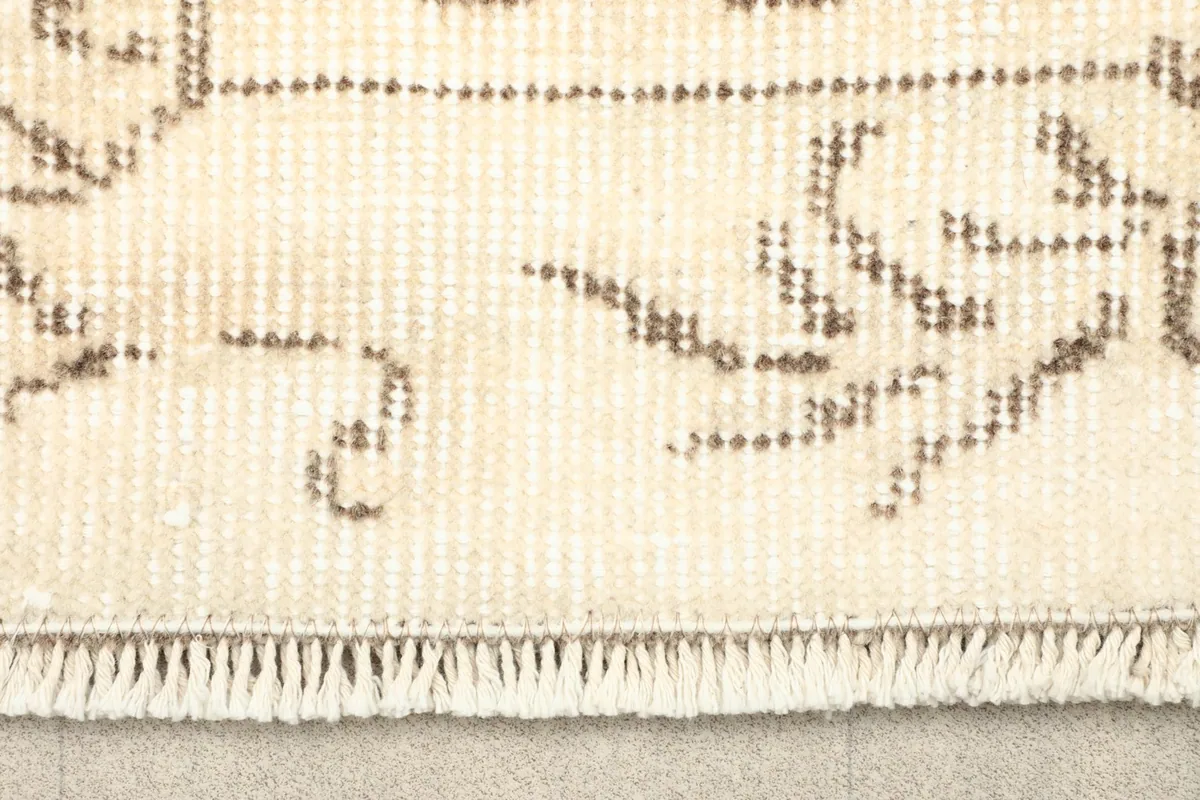 Close-up view of the rug's fringe and a faded beige geometric pattern.