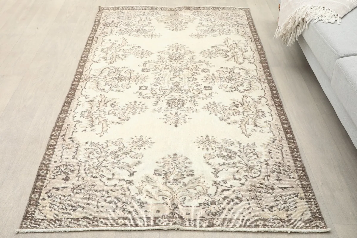 Ivory and brown floral vintage rug displayed in a room setting with a light-colored sofa and wood floor.