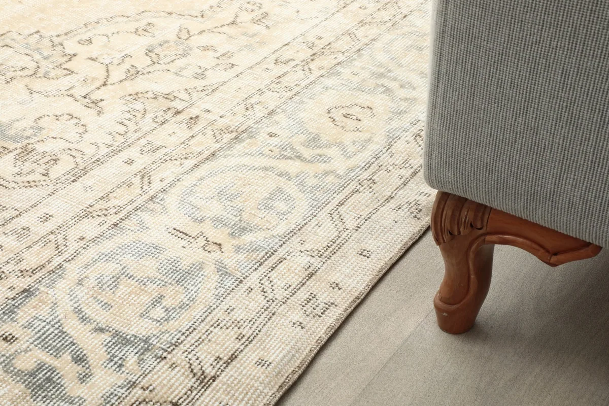 Close-up of the rug's edge next to a wooden sofa leg, showing pile and color variation.