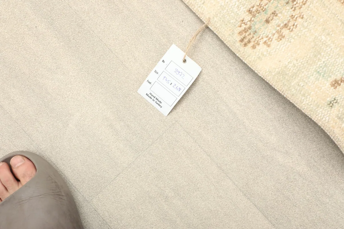 Overhead view of a foot and the RugsKilim tag on the floor next to the rug