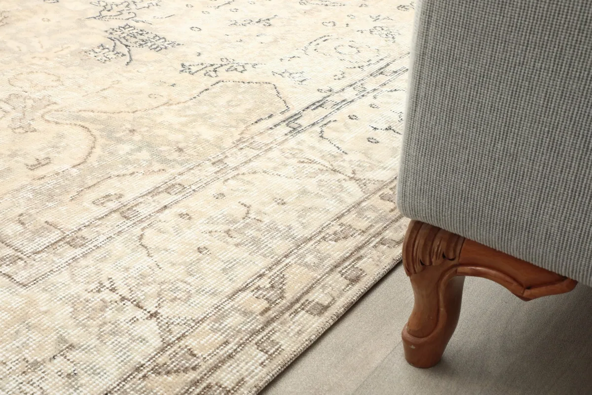 Close-up of the rug's pattern and border next to a sofa leg, showing texture and scale