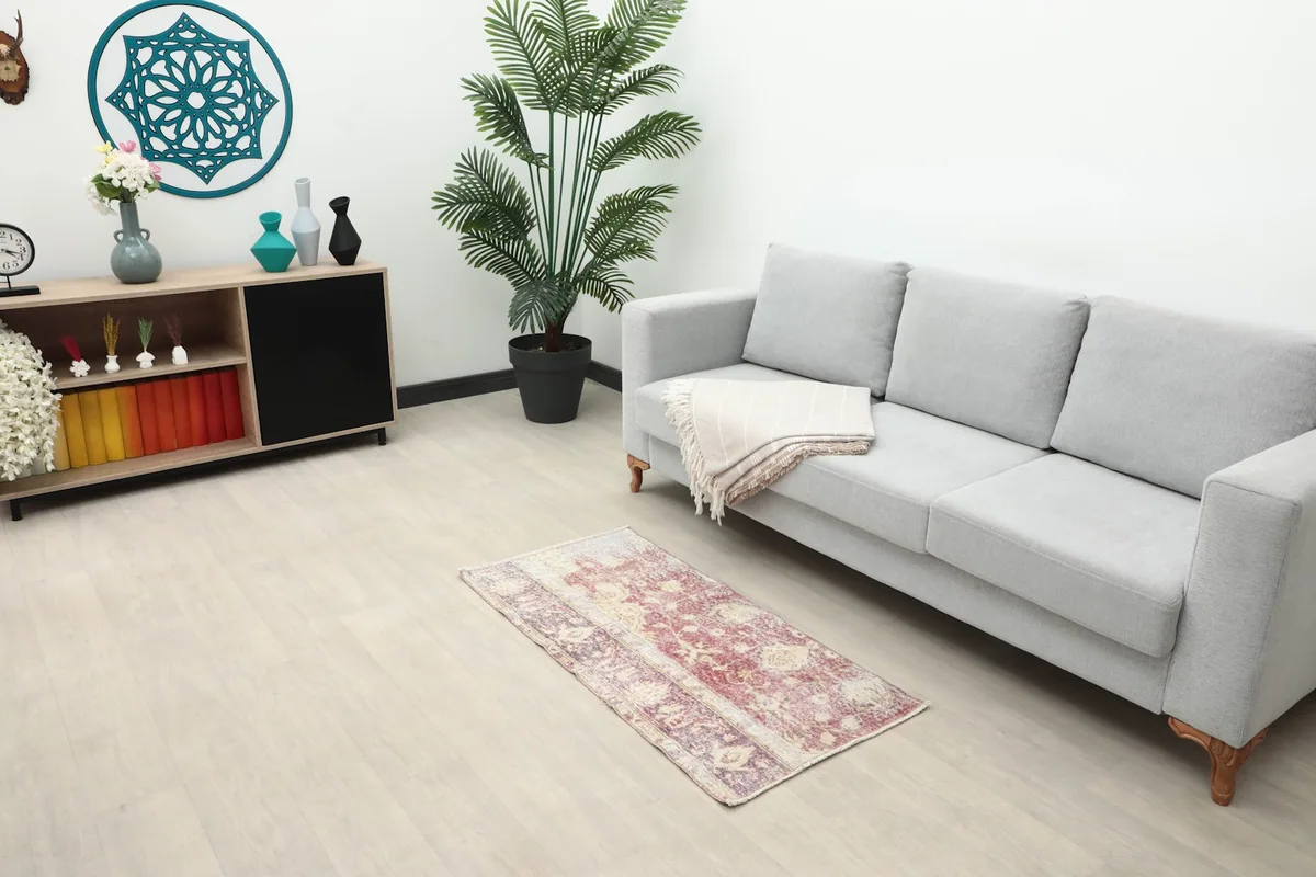 Vintage rose and purple rug placed in a living room setting next to a gray sofa.