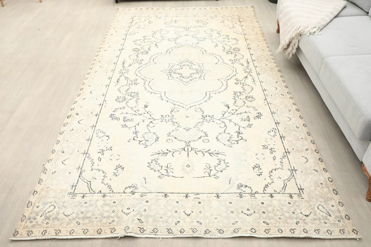 Overhead view of the 5'5" x 9'9" cream and charcoal rug laid out on a light floor next to a sofa.