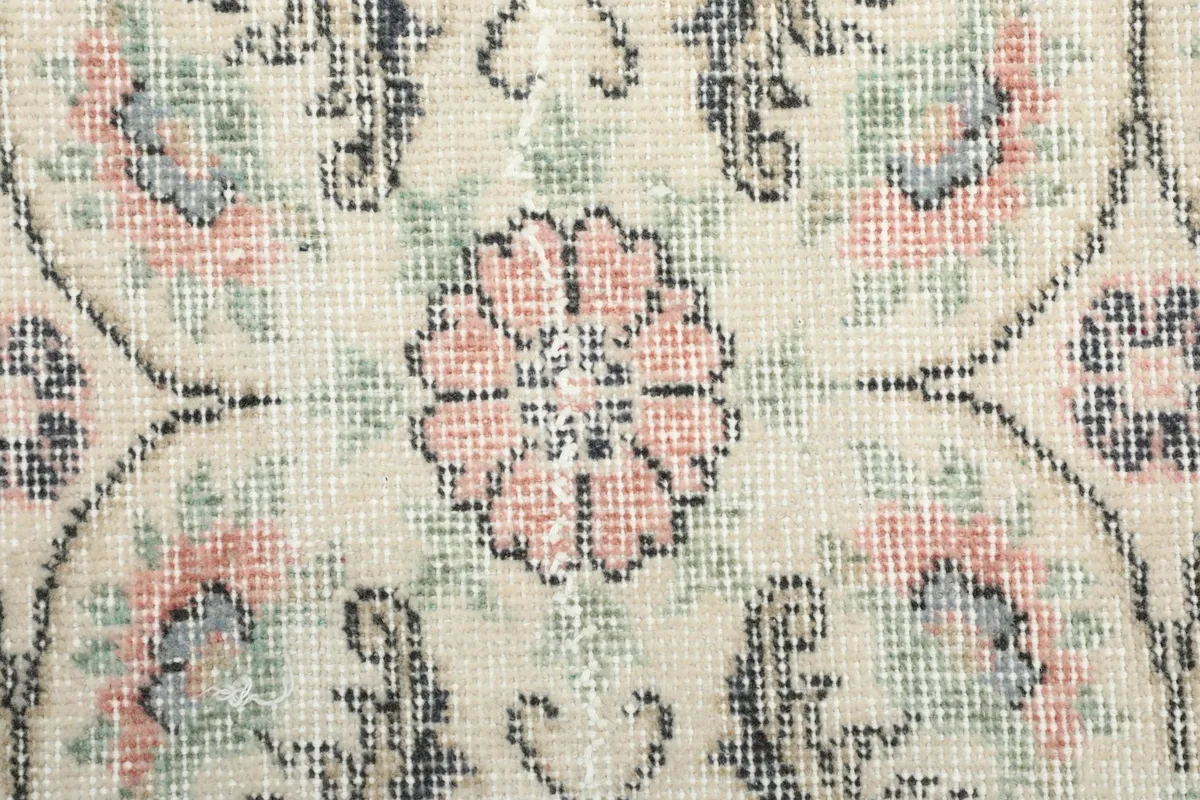 Close-up of a single rose-colored floral medallion within the ivory rug's pattern