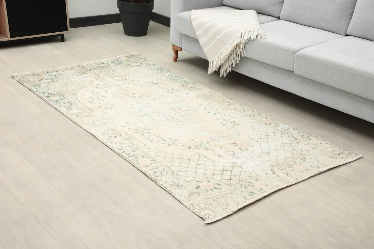 Close-up angled view of the ivory floral rug in a room setting, showing its faded colors.