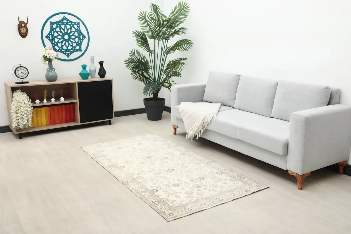 Small ivory rug placed in a living room scene with a gray sofa and wooden cabinet.