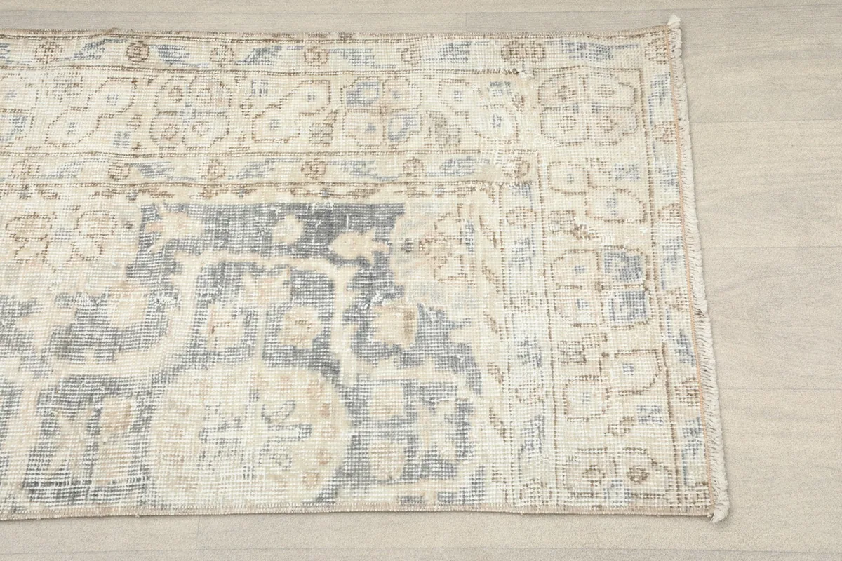Close-up detail of the rug's border and central floral and geometric motifs in beige and gray.