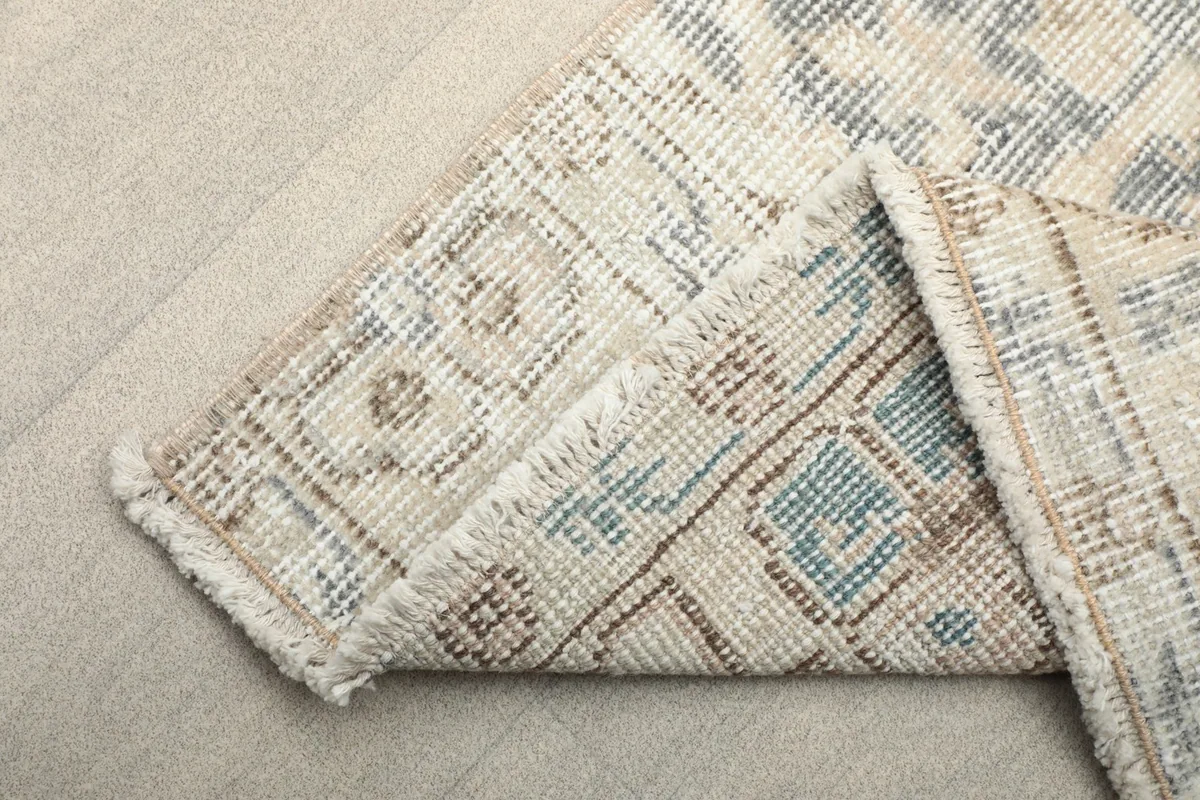 Folded corner of the rug revealing the cotton foundation and the reverse side of the knots.