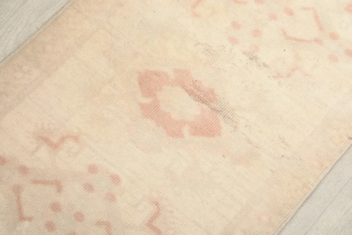 Detailed view of the wool pile and faded rose geometric design elements on the cream background.