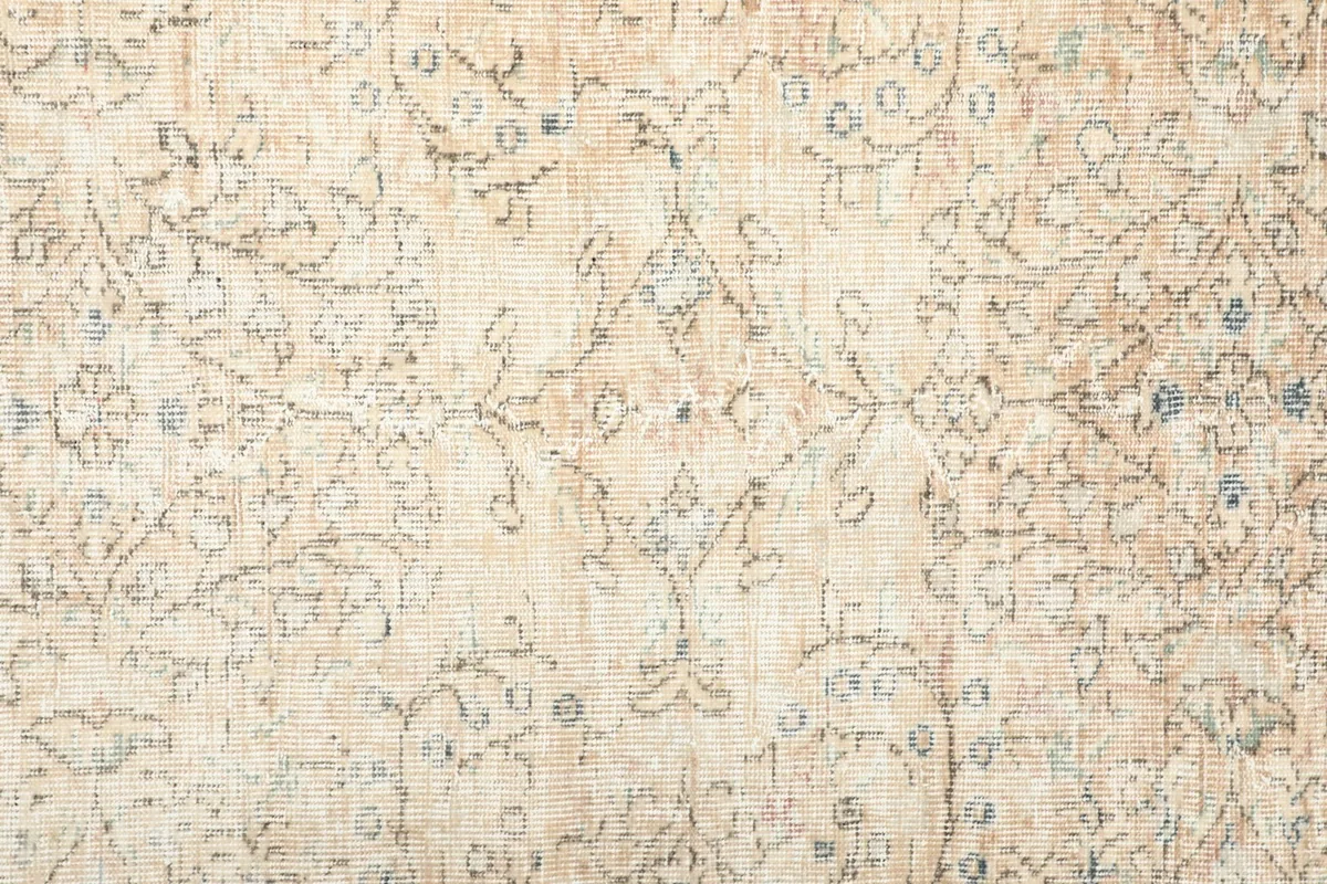 Detailed view of the rug's central field, showing faded ivory, tan, and blue floral patterns.
