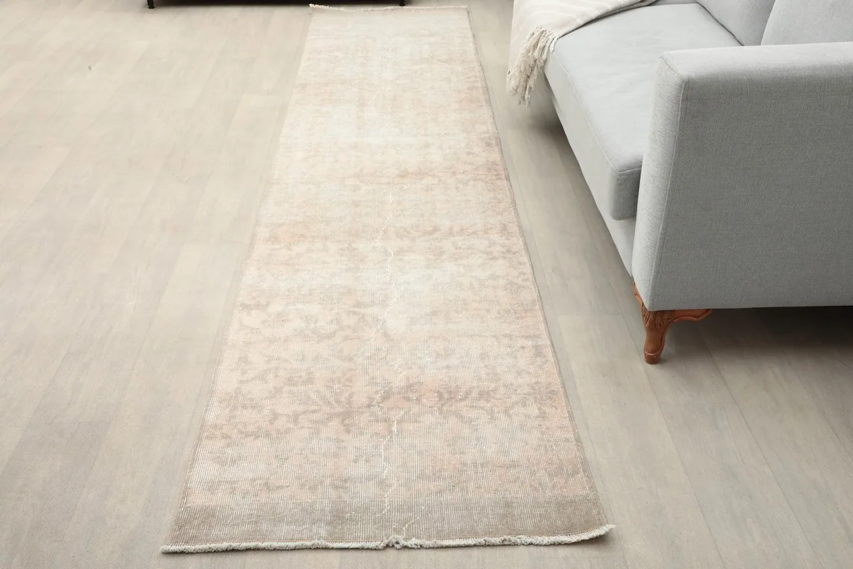 Runner rug placed in a living room setting next to a gray sofa, showing its length and neutral tones.