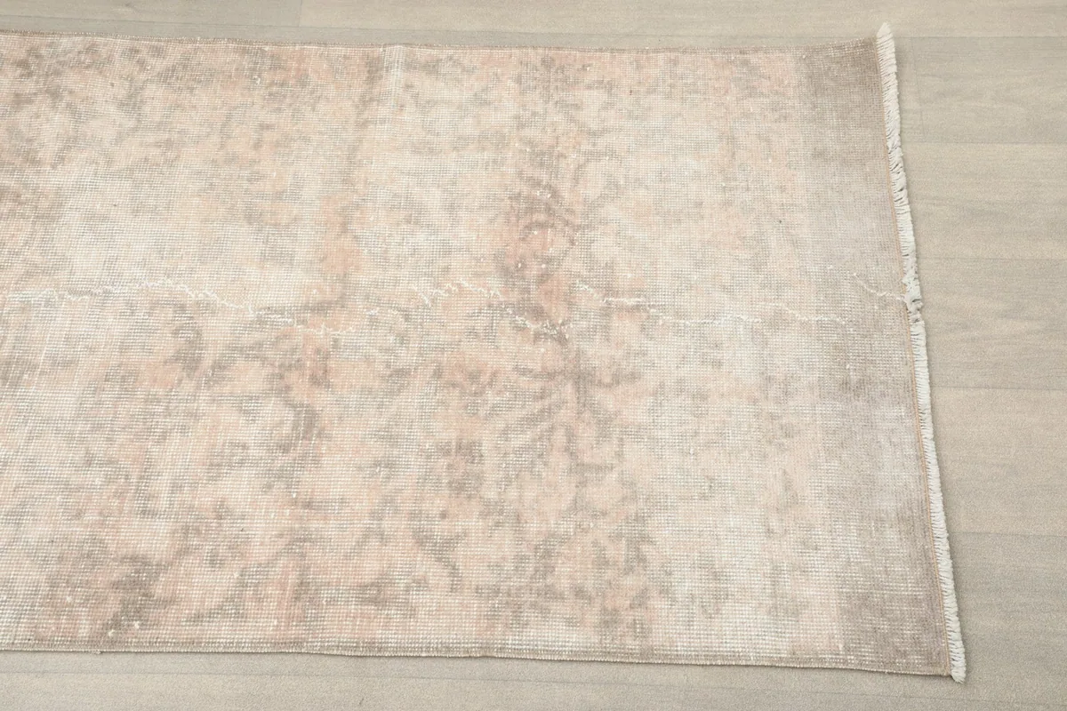 Close-up view of the rug's surface, revealing the faded floral patterns and blend of beige and cream colors.