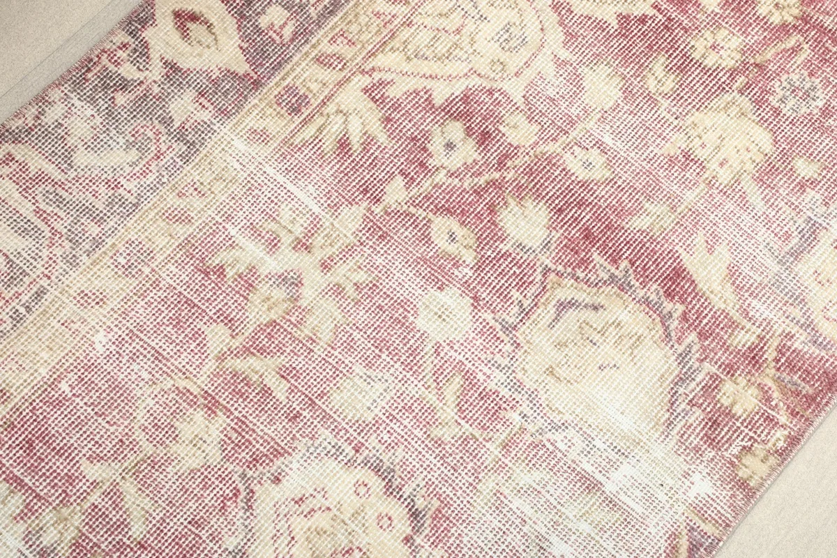 Macro view of the low wool pile, showing the hand-knotted texture and color variations of the rose and ivory threads.