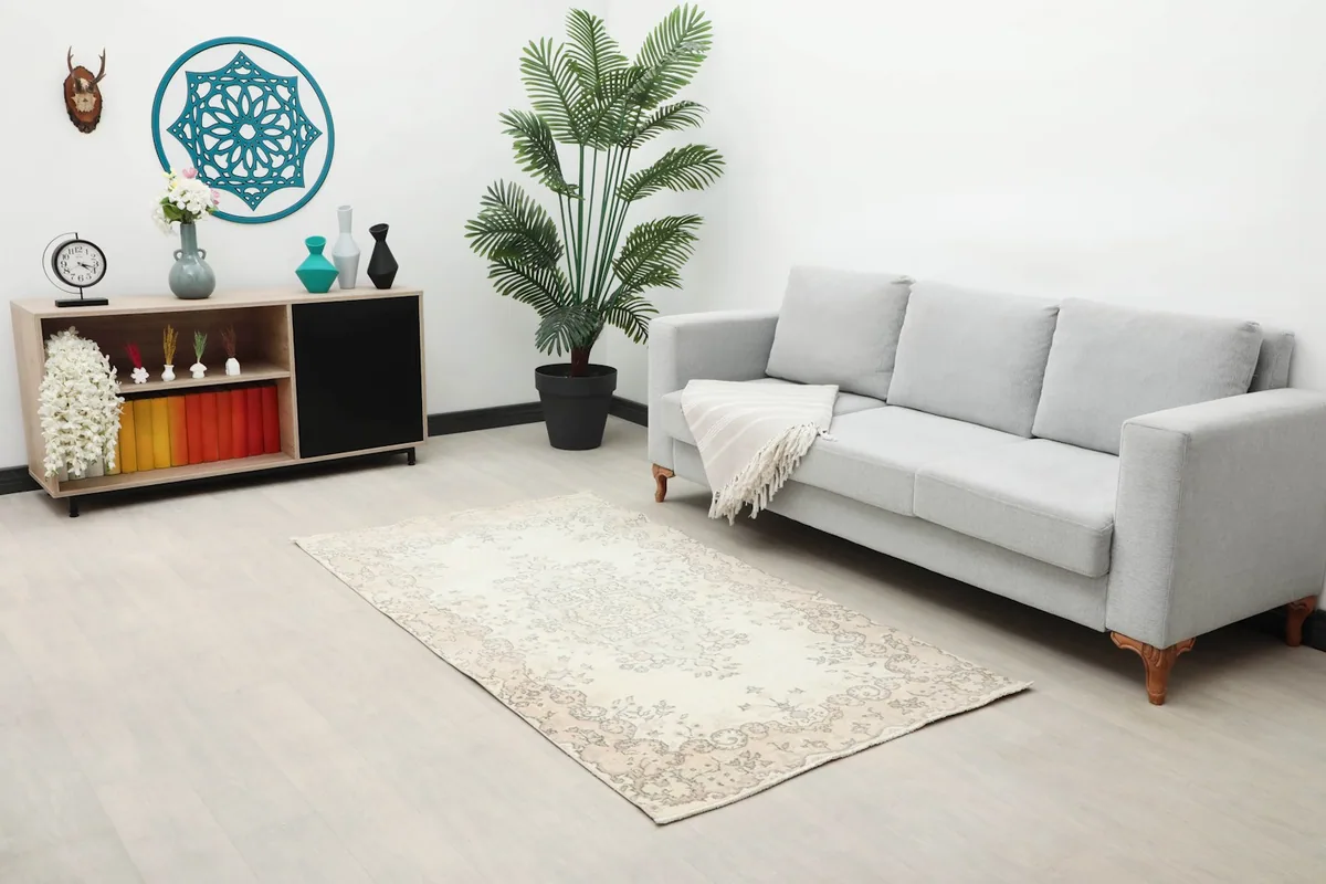 The ivory and beige vintage rug positioned in a living room next to a light gray sofa and a wooden cabinet.