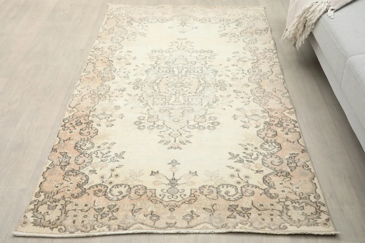 Overhead view of the ivory and beige vintage rug in a room setting on a light wood floor, showing its overall appearance.