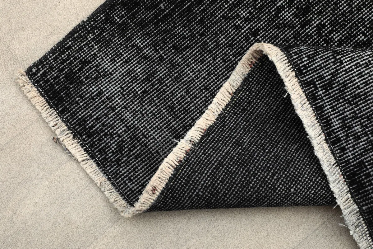 Folded corner of the rug revealing the short, natural-colored fringe and cotton foundation