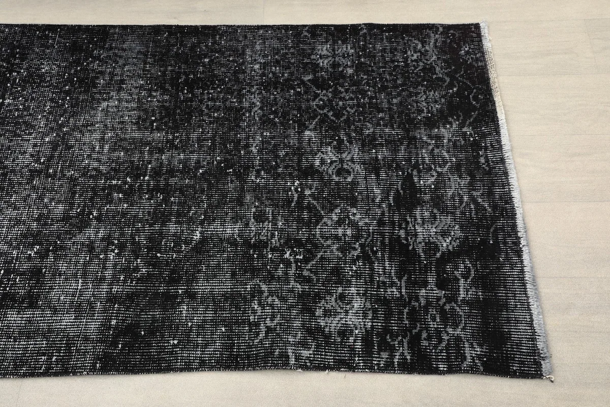 Overhead view of one end of the black runner rug, showing the faded geometric pattern and fringe.