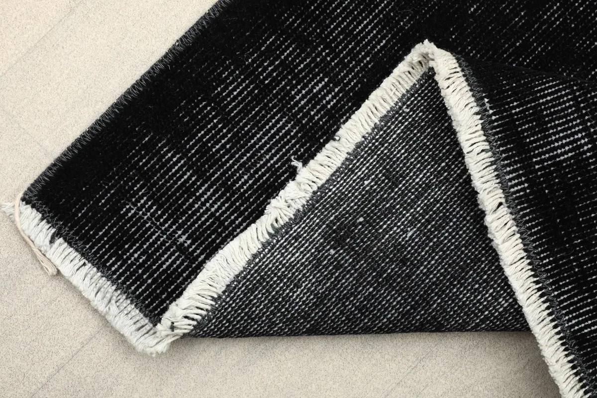 Corner of the rug folded to show the cotton foundation and reverse side