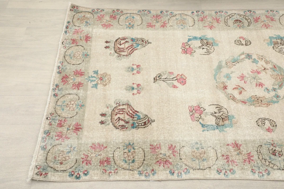 Angled shot of the rug's surface, showing the subtle color variations and the detailed floral border.