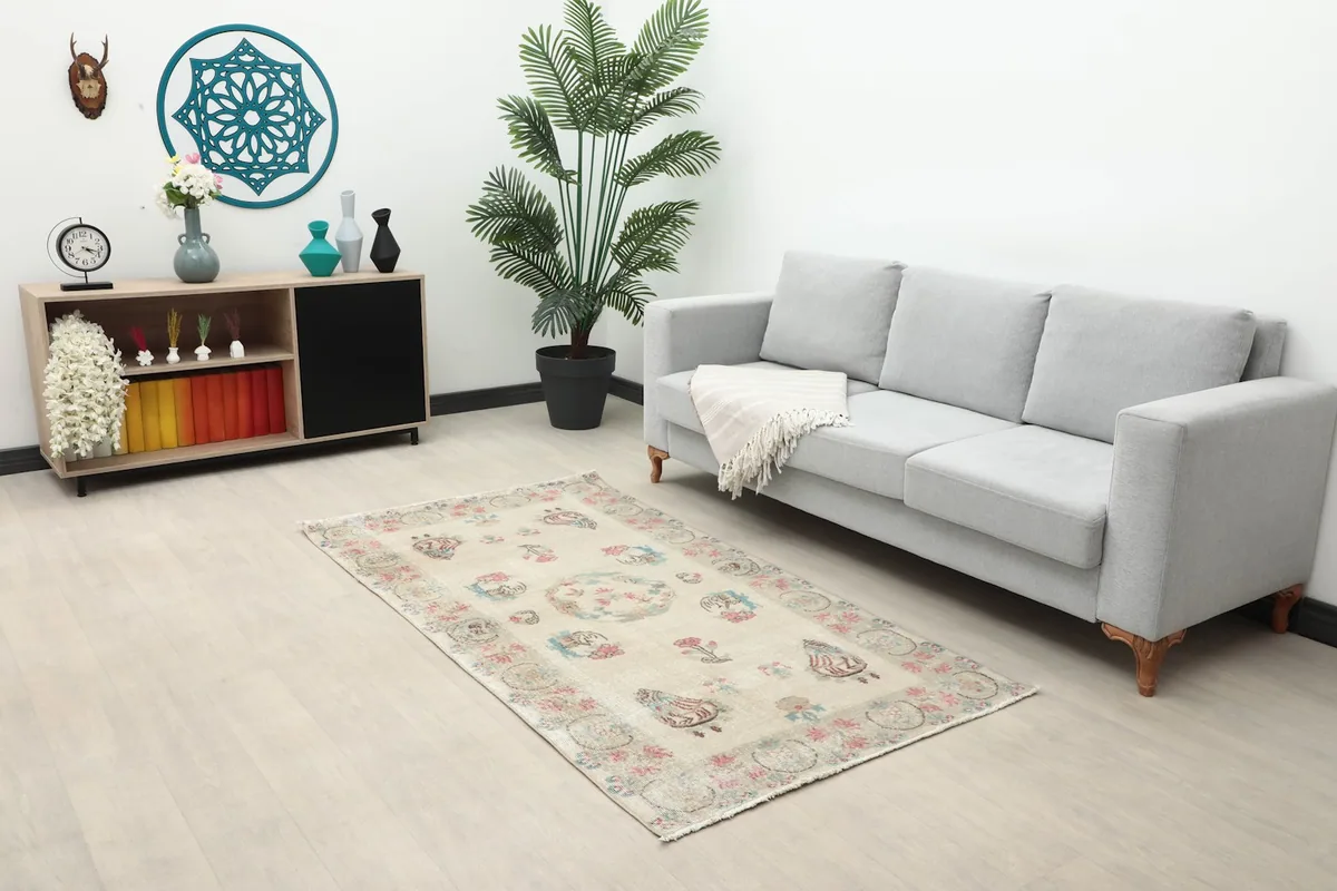 The beige vintage rug displayed in a living room setting, complementing a gray sofa and light wood furniture.
