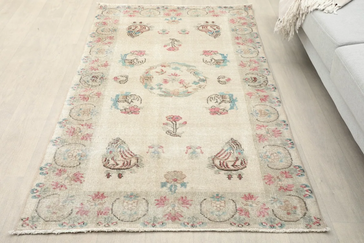 Overhead view of the beige rose floral medallion rug on a light wood floor next to a sofa.
