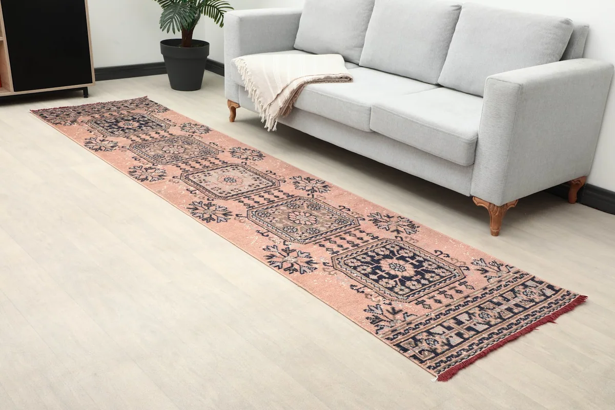Angled view of the rose and navy runner rug extending along a light-colored floor next to a sofa.