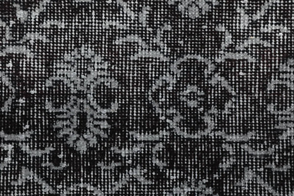 Macro shot of the hand-knotted texture and intricate, faded floral motifs in gray and black