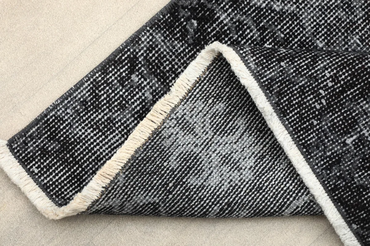 Corner of the rug folded back, showing the cotton foundation and the short white fringes