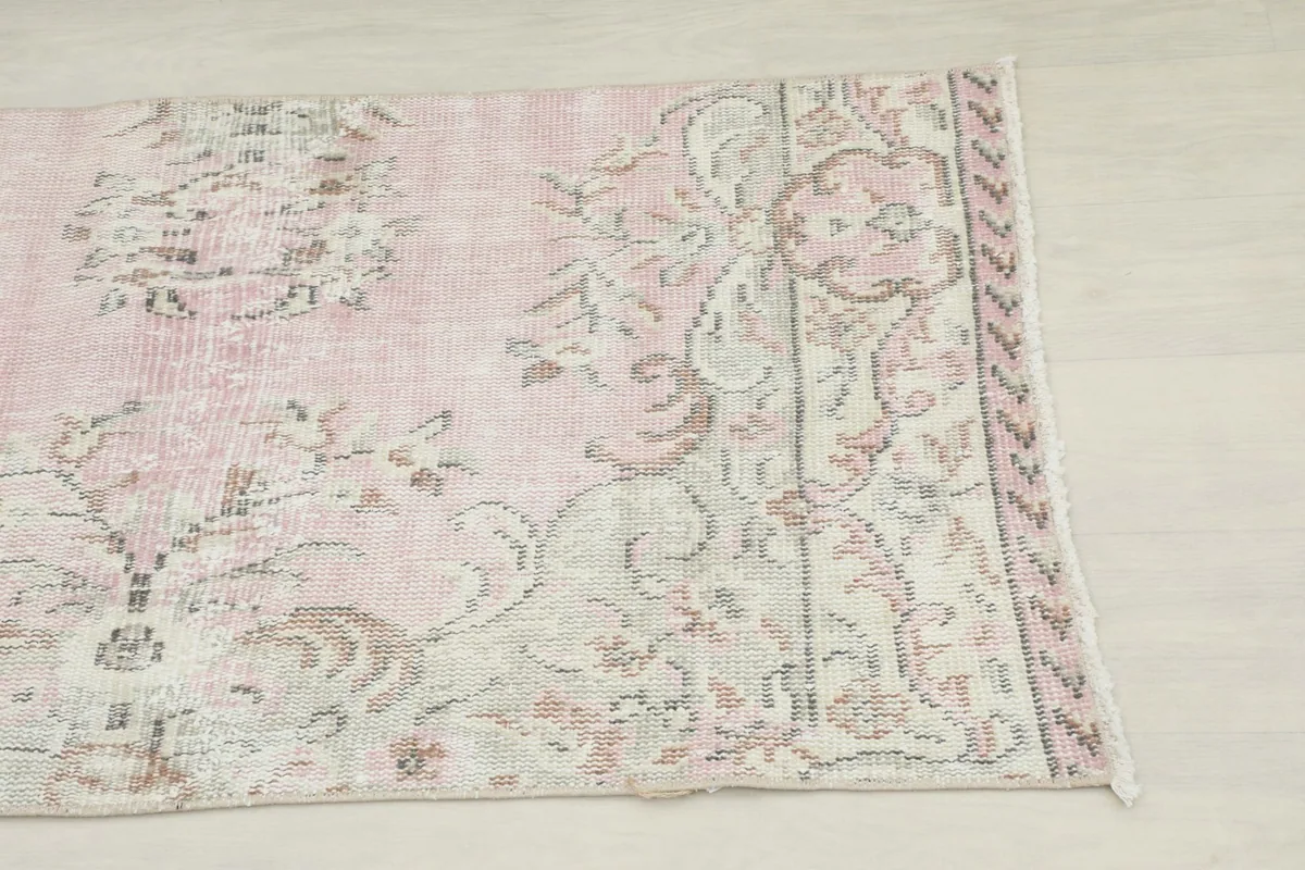 Close-up detail of the rug's corner showing the floral pattern and border in rose, beige, and olive