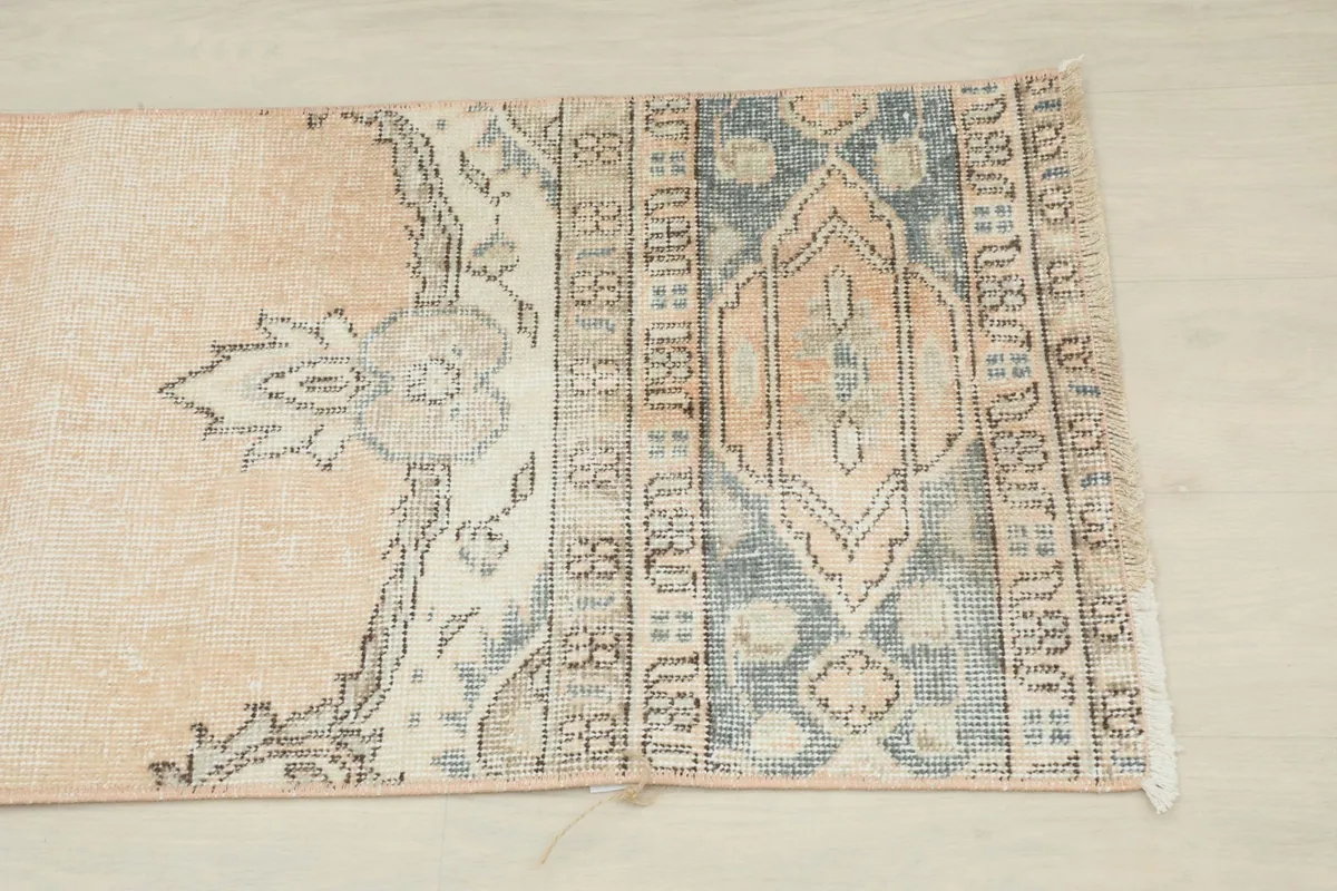 Close-up of the rug's end, showing the blue and cream geometric border and faded beige field.