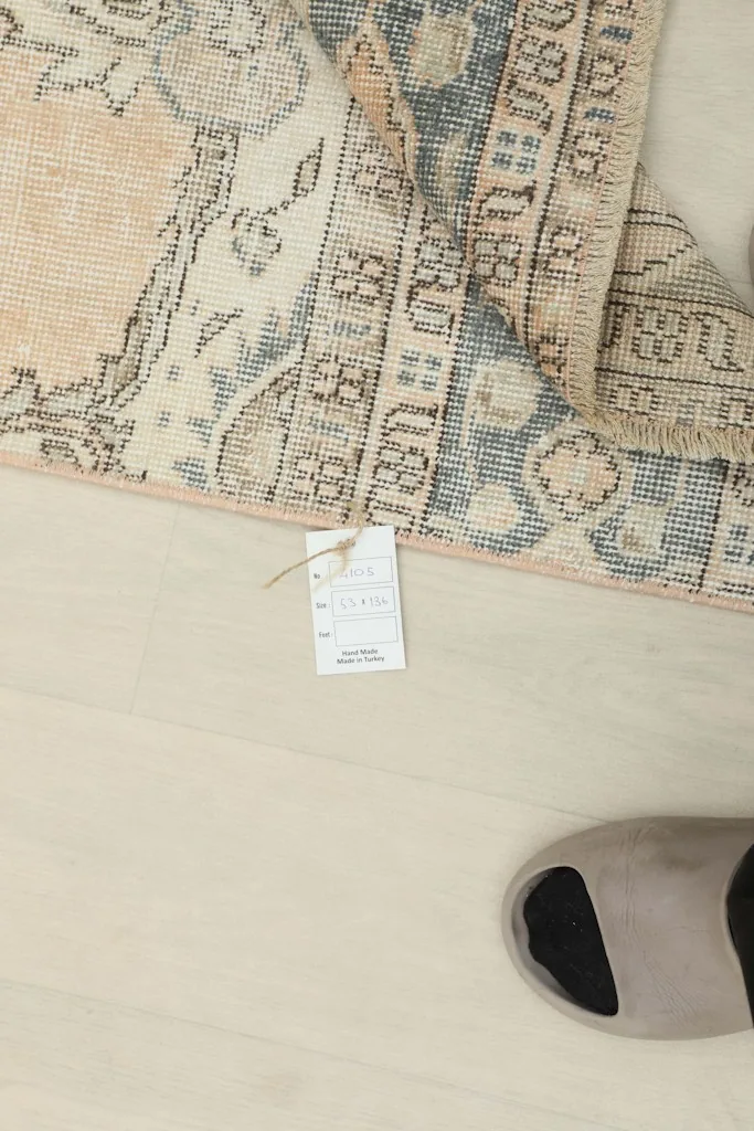 Rug corner with a product tag, indicating its origin and material, next to a slipper for scale.