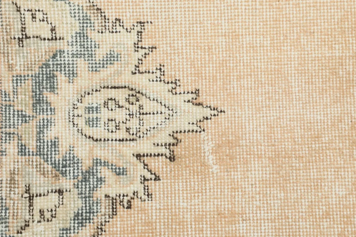 Macro detail of the beige field and a faded blue floral motif, showing the low pile texture