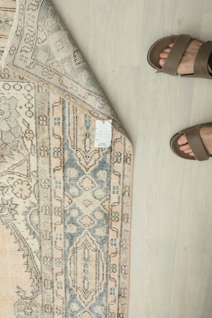 Overhead view showing the rug's back with a tag, alongside a person's feet for scale.