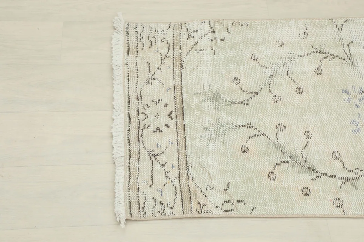 Detail of the rug's border and fringe, showing the faded brown and cream patterns.