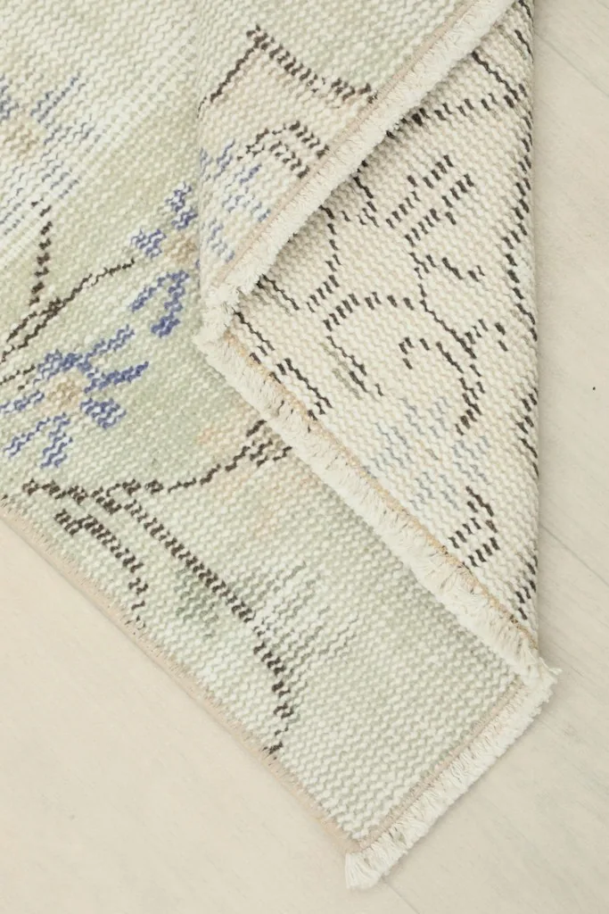 Corner of the rug folded back, revealing the cotton foundation and tight knotting.