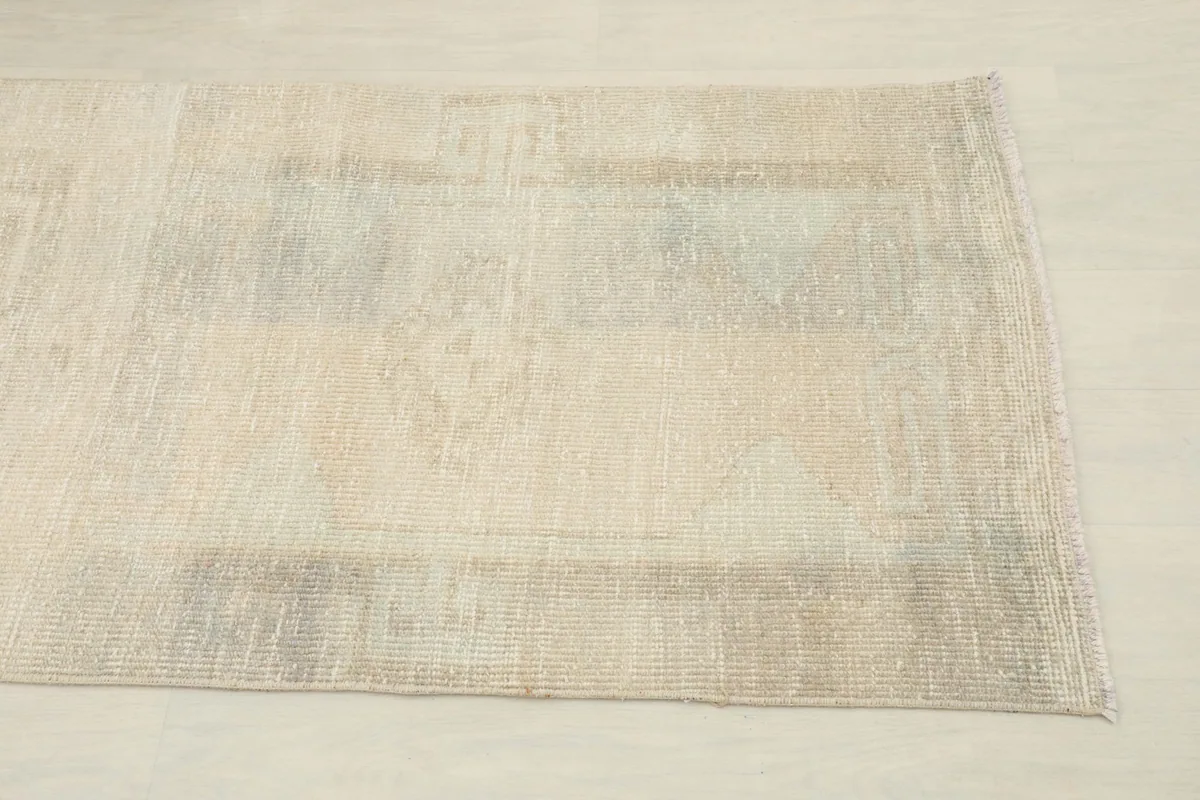 Close-up of the rug's end, showing subtle beige and gray tones with faded patterns