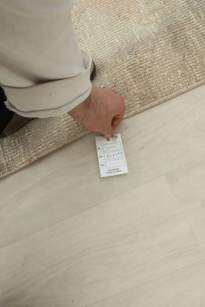 A hand holding the product tag, showing details of the vintage Anatolian runner