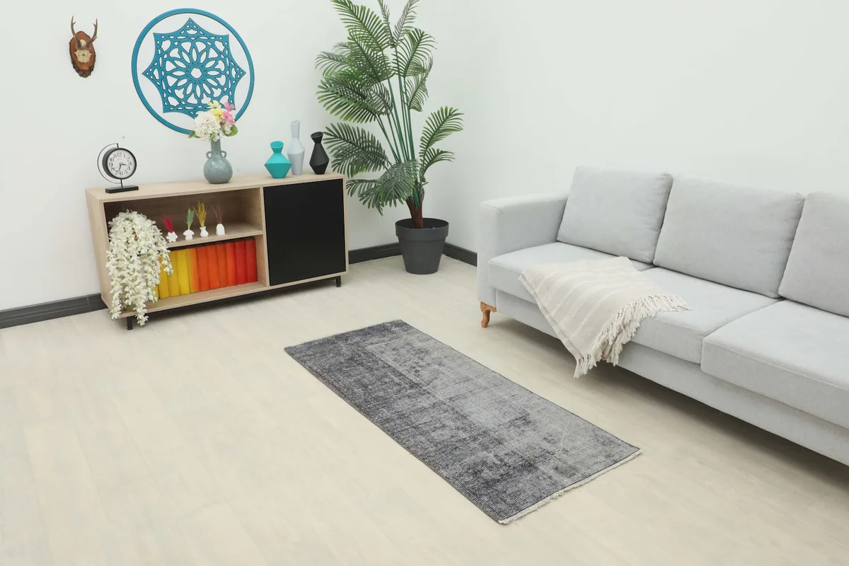 Charcoal and gray vintage area rug placed in a modern living room setting with a light gray couch and wooden cabinet.