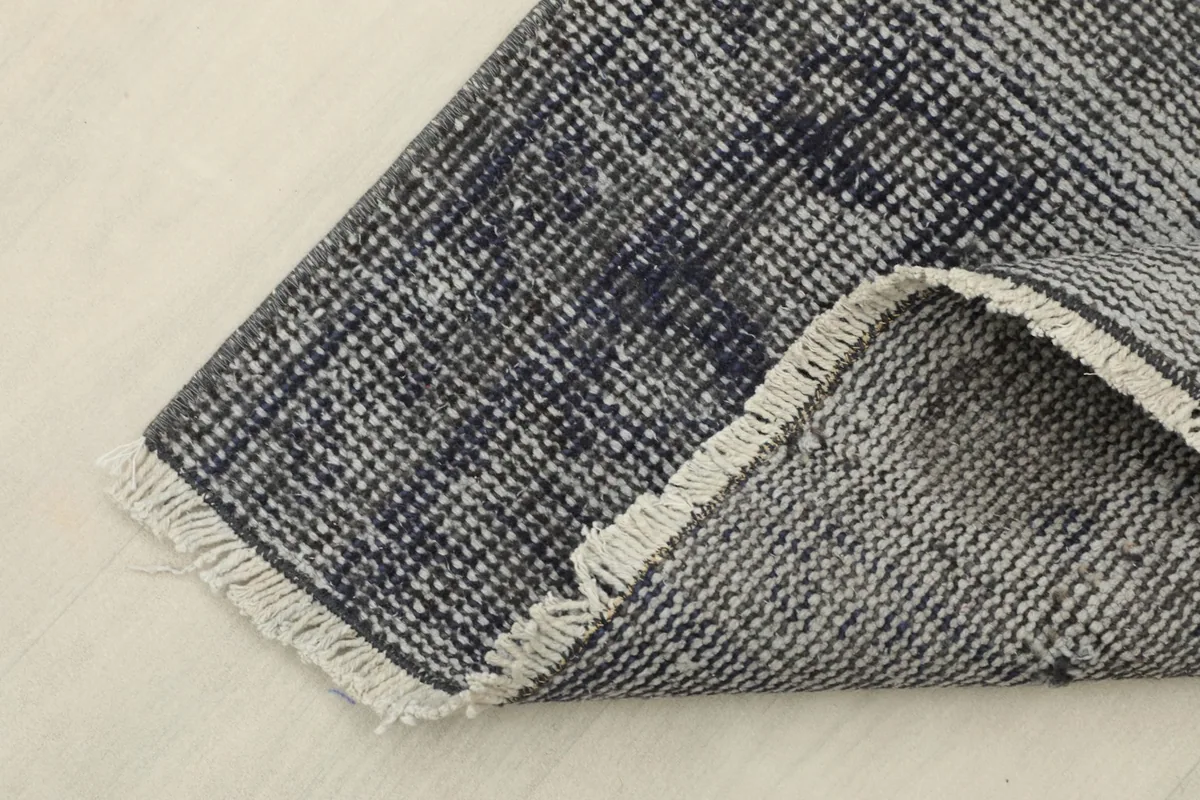 Close-up of the folded corner, revealing the reverse side of the hand-knotted wool rug and fringe detail.