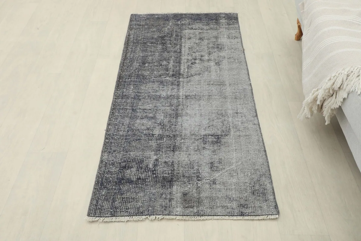 Overhead view of the charcoal and gray vintage rug in a room setting, next to a light gray couch.