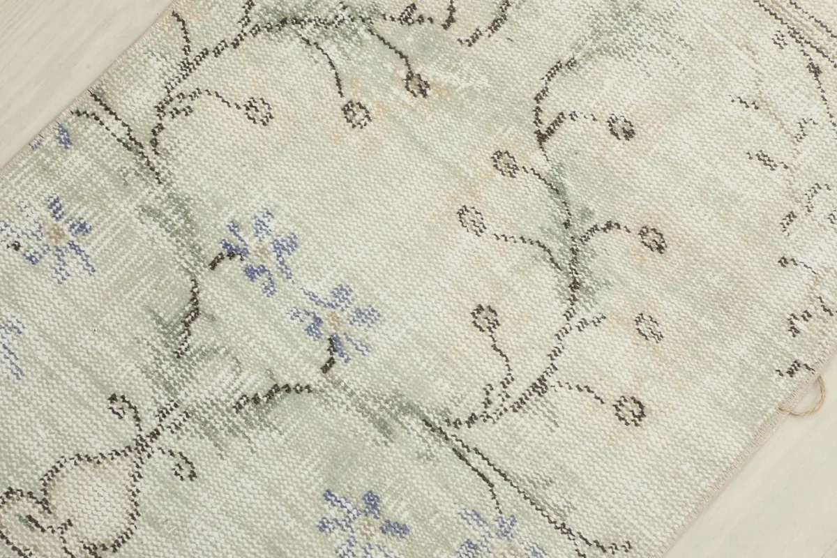 Detailed view of the wool pile and distressed blue floral motifs on a cream background