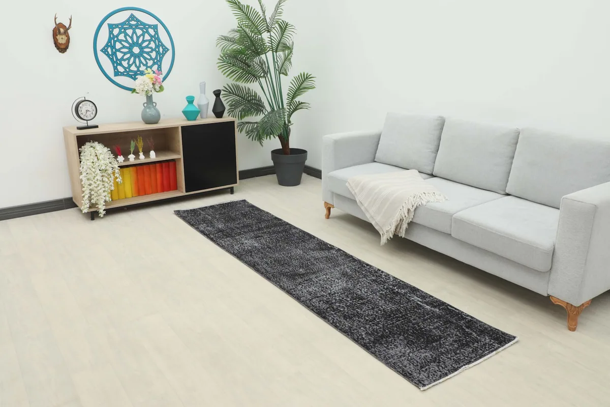 Vintage charcoal runner rug placed in a modern living room setting next to a light gray sofa and wooden cabinet.