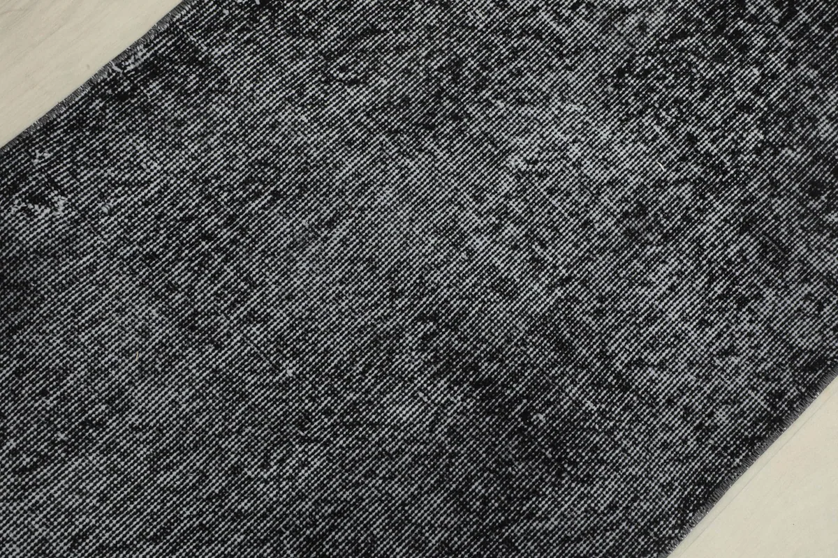 Detailed view of the distressed wool pile, showing the interwoven charcoal and gray threads of the vintage rug.